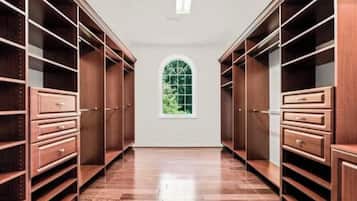 A walk-in closet with wooden shelving and drawers, a large arched window, and a polished wooden floor.