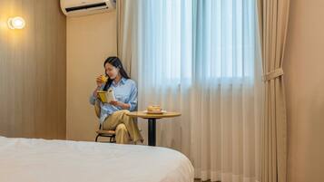 A hotel room with a bed, a small table with a sandwich, and a person reading a book.