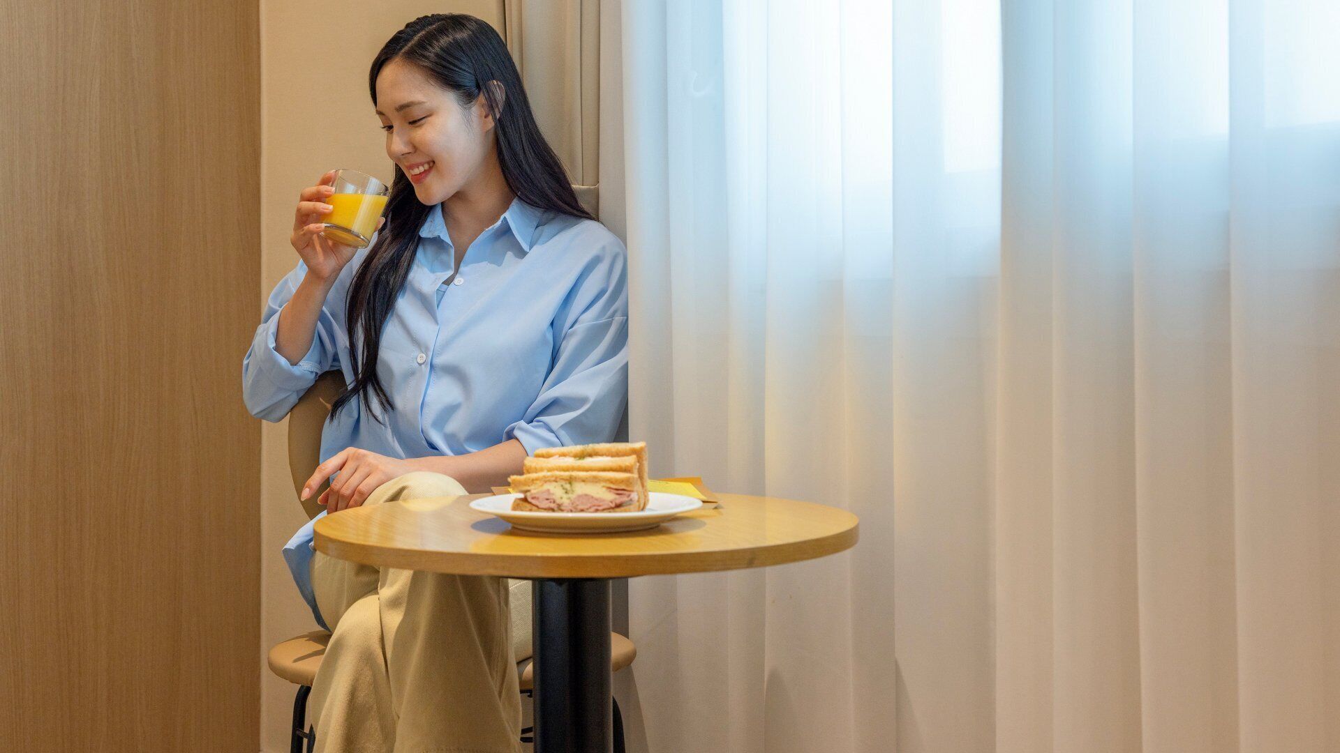 A person sitting at a round table with a sandwich and a glass of orange juice.
