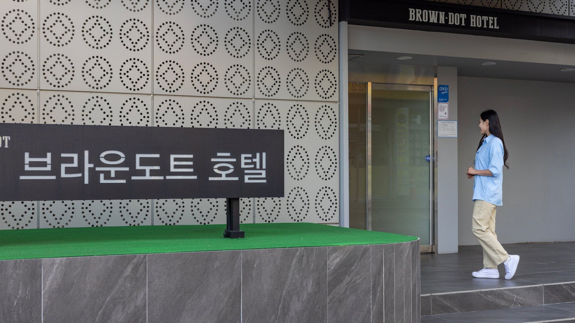 A hotel entrance with a sign in Korean, a patterned wall, and a person walking.