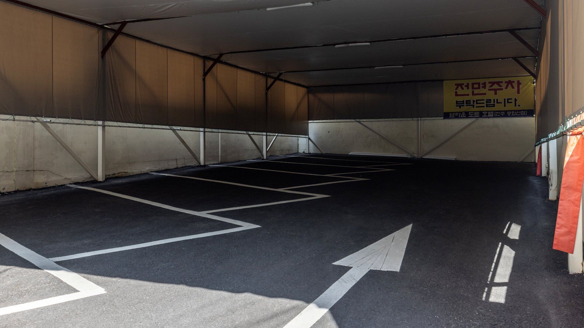An empty parking garage with marked parking spaces and directional arrows on the floor.