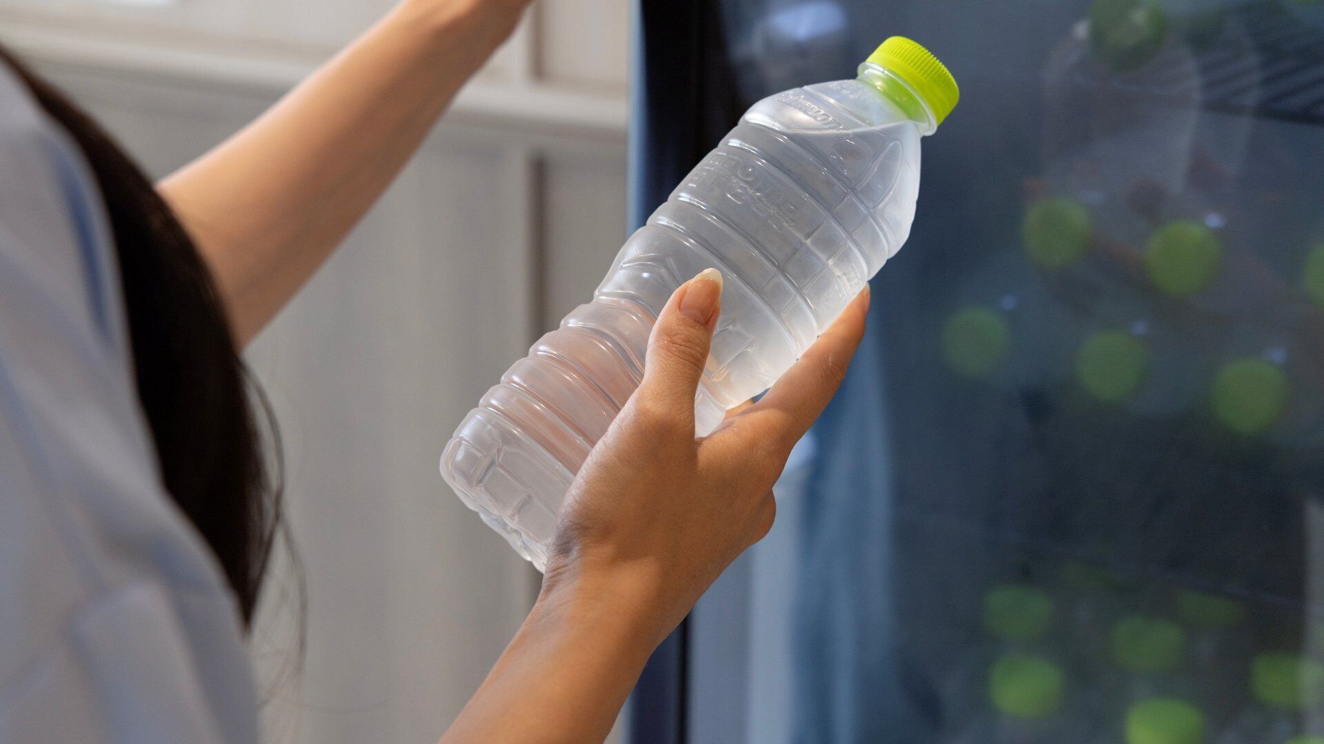 Uma pessoa segurando uma garrafa de água de plástico transparente com tampa verde.