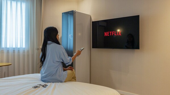 A person sitting on a bed using a remote control, with a TV displaying the Netflix logo on the wall.