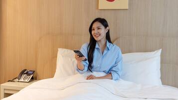 Ein Hotelzimmer mit einem Bett, weißer Bettwäsche, einem Nachttischtelefon und einem an der Wand befestigten Kunstwerk.