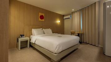 A hotel room with a large bed, a bedside table with a phone, a wall-mounted air conditioner, and a window with curtains.