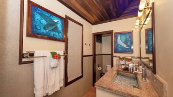 Une salle de bain avec un plafond en bois, un lavabo doté d’un plan de travail en granit et deux œuvres d’art encadrées au-dessus du miroir.
