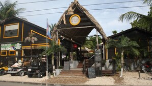 A restaurant with a thatched roof, outdoor seating, and a sign advertising a pool bar.