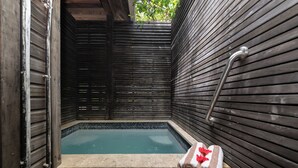 A wooden deck leading to a small, enclosed hot tub area with a metal handrail and a towel on the floor.