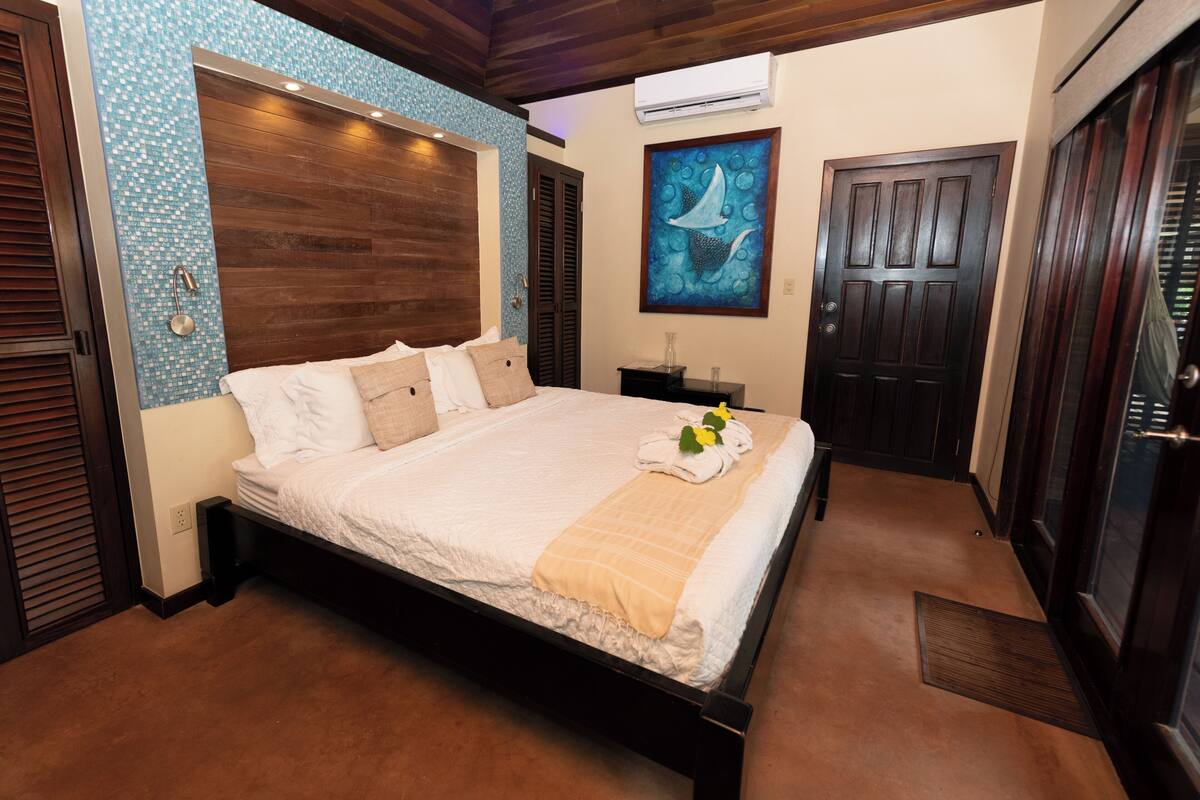 Une chambre à coucher avec un lit, une tête de lit en bois, un tableau, une porte et une fenêtre.