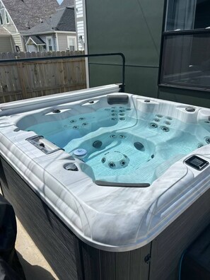 A hot tub with a control panel and jets, surrounded by a wooden deck and a house in the background.