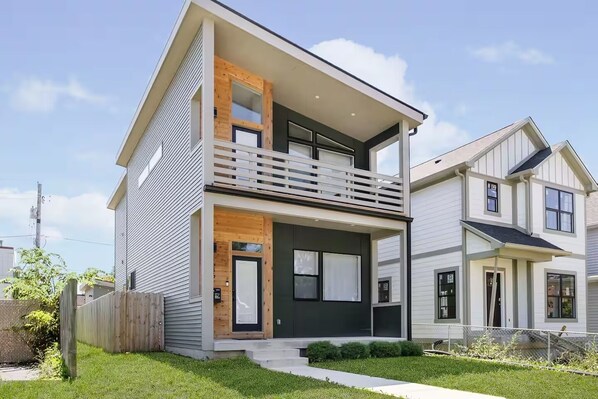 A modern two-story house with a balcony, a front porch, and a well-maintained lawn.