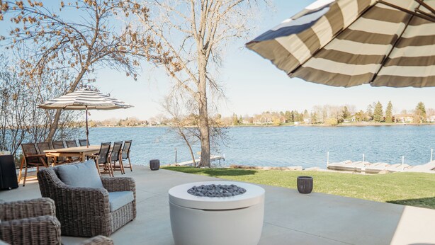 Un patio al aire libre con mobiliario de mimbre, una mesa redonda con un centro de guijarros y vista a un lago.