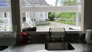 A kitchen with a stainless steel sink, a coffee maker, and a window overlooking a garden and a house. - Valmai House & Motel (Cambridge)