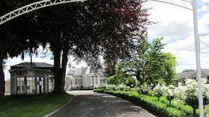 A street with a gazebo, a building with a white facade, and a row of white flowering bushes. - Valmai House & Motel (Cambridge)