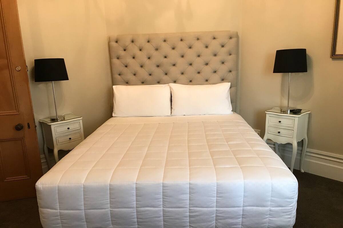A neatly made bed with a quilted white duvet, two bedside tables with lamps, and a tufted headboard.