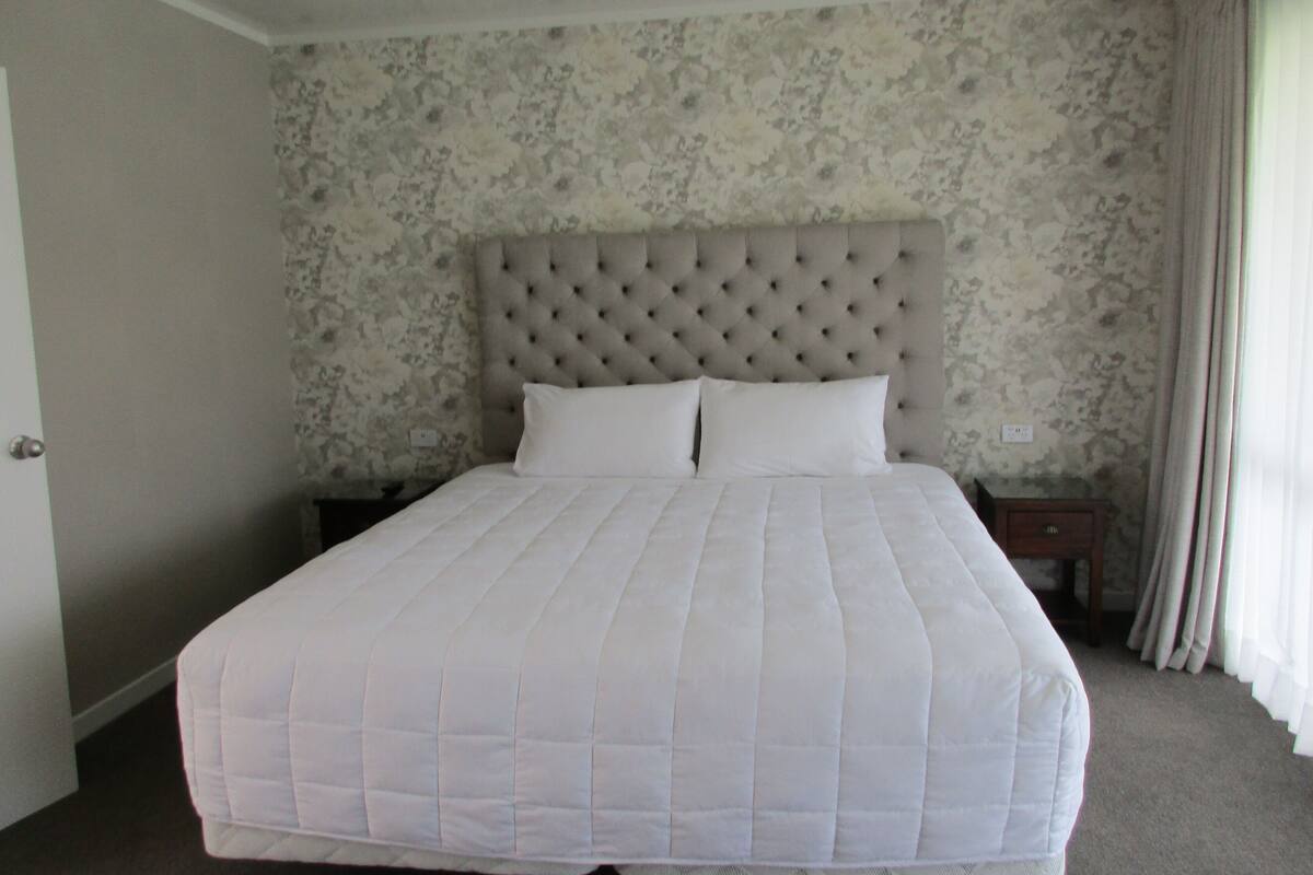 A large bed with a tufted headboard in a room with floral wallpaper.