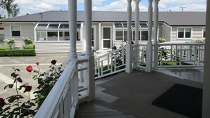 A covered porch with white railings and columns, leading to a house with a grey roof and multiple windows. - Valmai House & Motel (Cambridge)