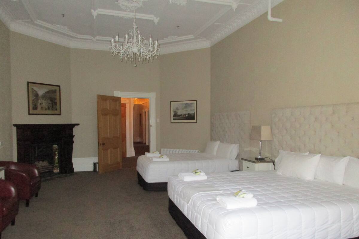 A hotel room with two beds, a chandelier, a fireplace, and framed pictures on the walls.