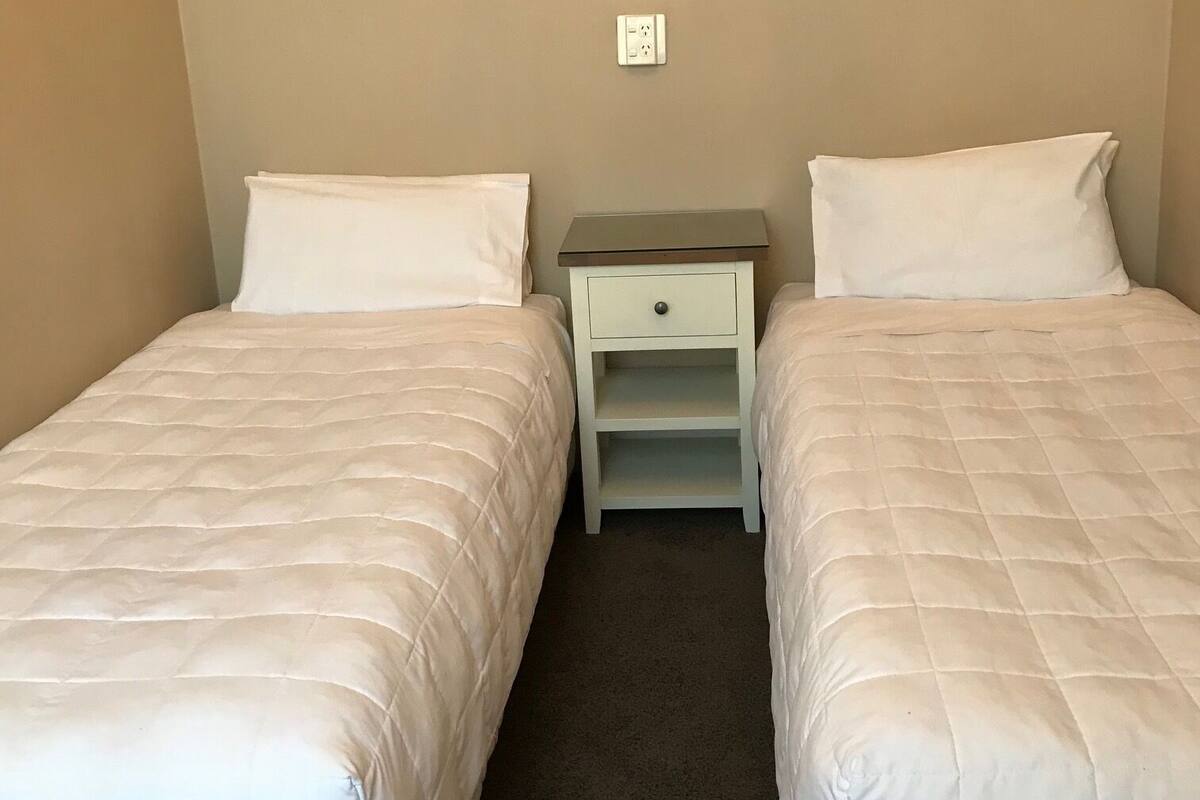 A twin room with two beds, a nightstand, and a power outlet on the wall.