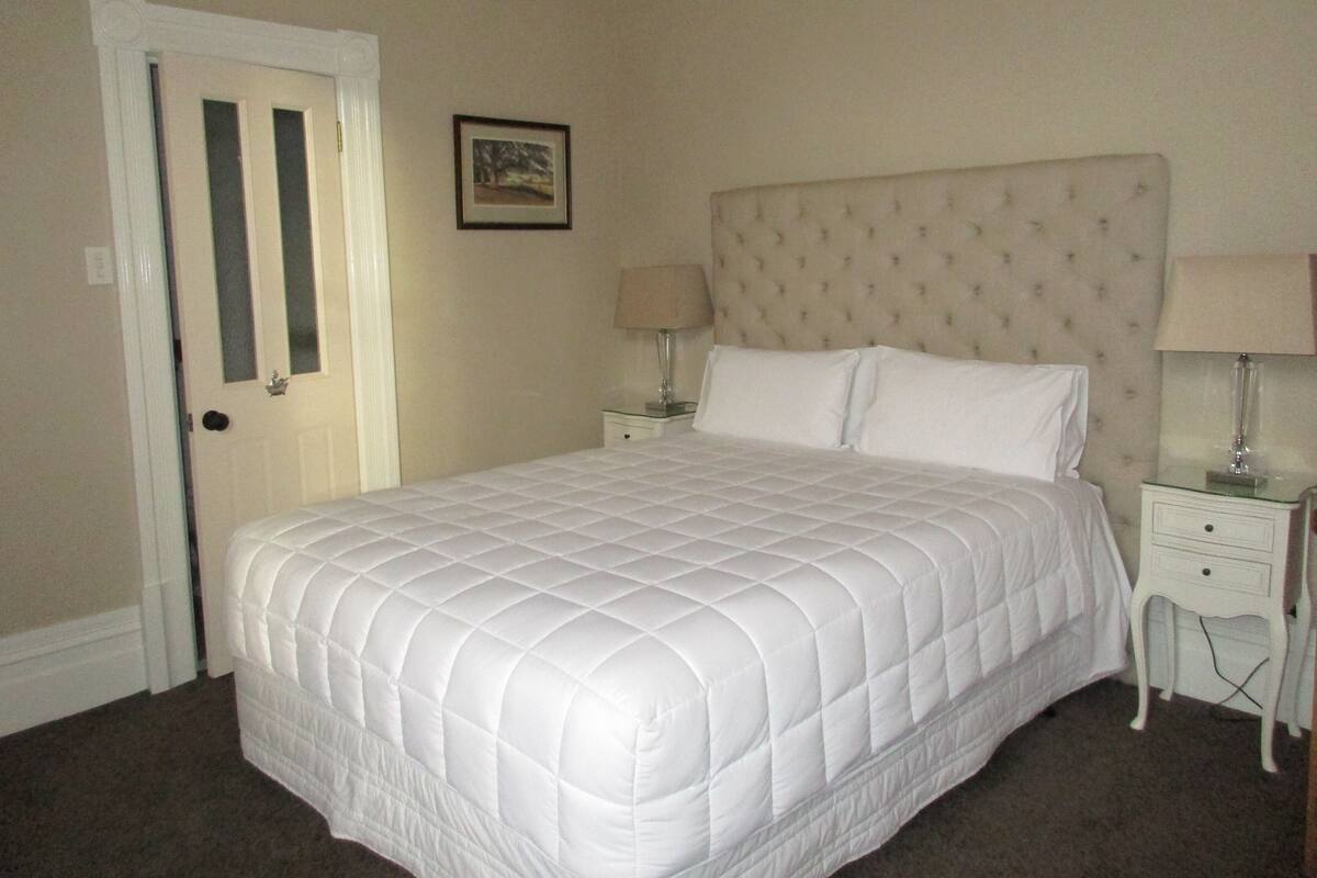 A neatly made bed with a quilted headboard, two bedside tables with lamps, and a framed picture on the wall.