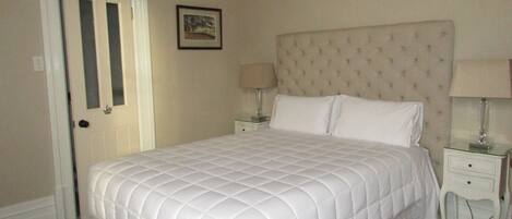 A neatly made bed with a quilted headboard, two bedside tables with lamps, and a framed picture on the wall.