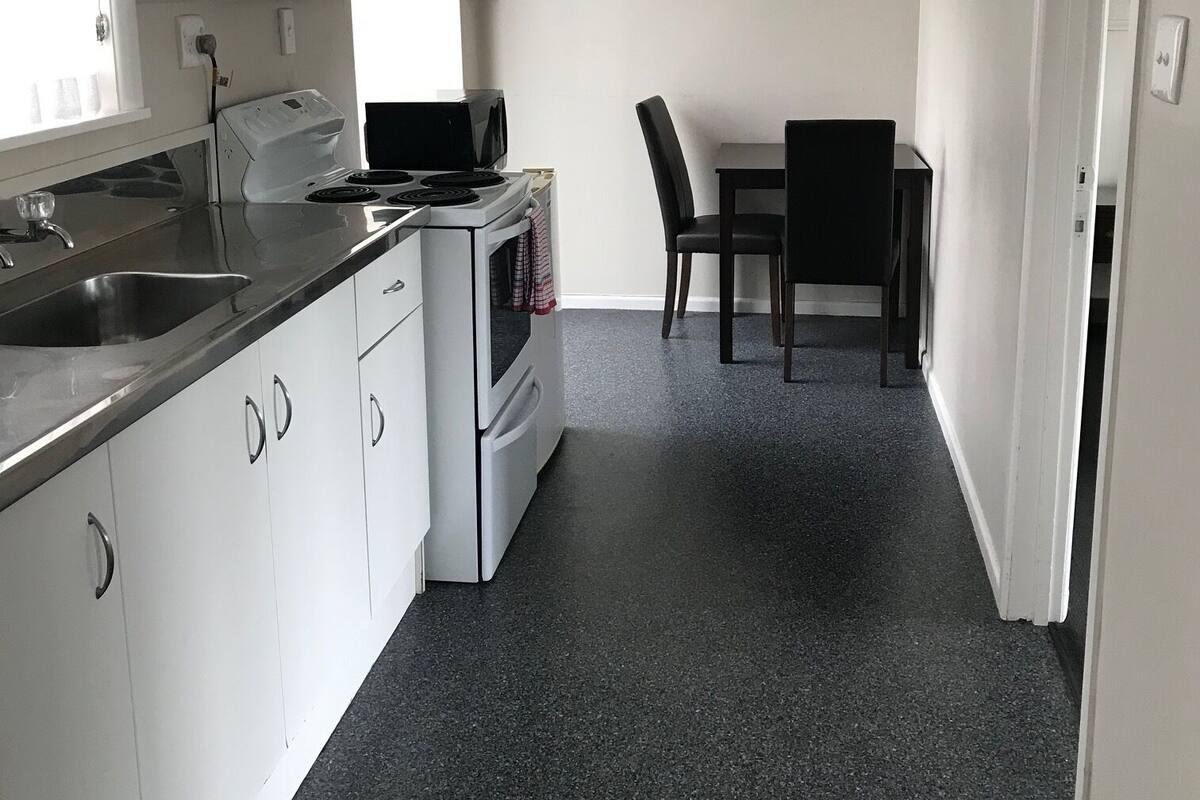 A compact kitchen with white cabinets, a stove, and a microwave. There is a dining area with a table and chairs.