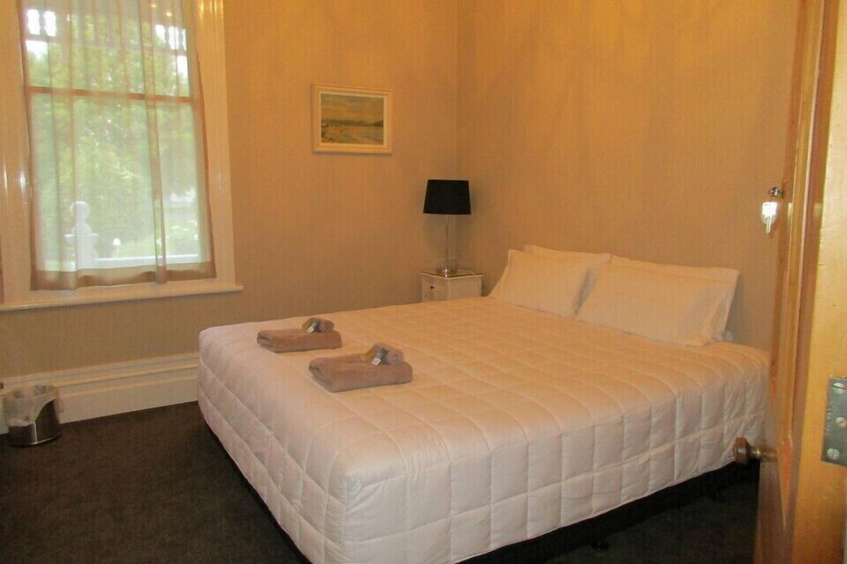 A neatly made bed with two towels, a bedside lamp, and a painting on the wall.
