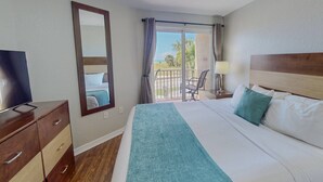 Habitación de hotel con cama, televisión, escritorio, silla, balcón con vistas y ventilador de techo.