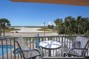 Un balcon avec vue sur une plage, une piscine et des palmiers.
