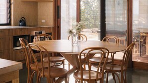 A modern kitchen with wooden cabinetry, a dining table with chairs, and a large window with a view of the outdoors. - Wildwood Barn: New Luxe Home, Valley Views, Outside Bath, Firepit & Ocean Views (Yallingup)