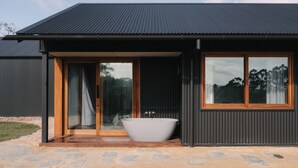 A modern house with a large bathtub outside, a sliding glass door, and a dark exterior. - Wildwood Barn: New Luxe Home, Valley Views, Outside Bath, Firepit & Ocean Views (Yallingup)