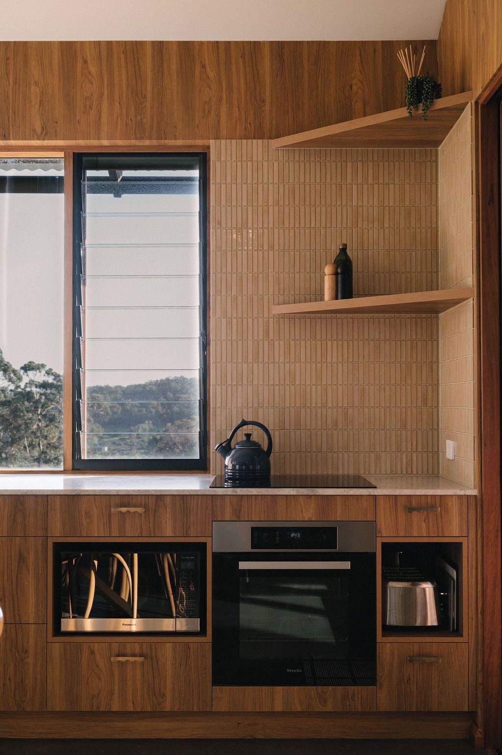 A modern kitchen with wooden cabinetry, a built-in oven, and a window overlooking a scenic view.