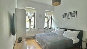 Ein Schlafzimmer mit einem Bett, einem Nachttisch, einer Lampe und einem Fenster mit Vorhängen.