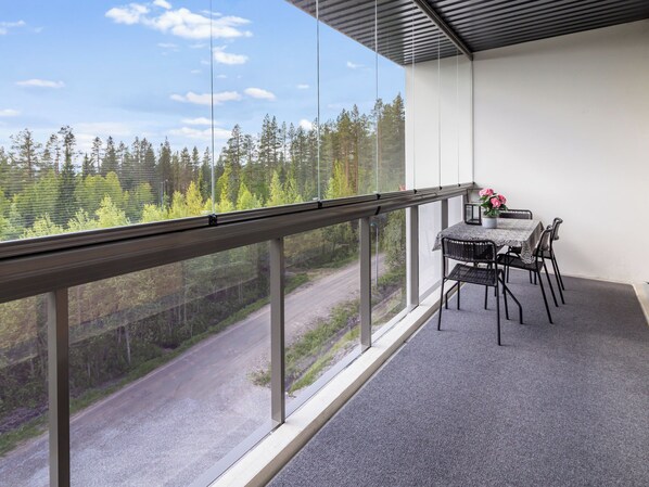 A balcony with a table and chairs, overlooking a forested area with a road. - Aurinkorinne 1 as 24 by Interhome (Kittilä)