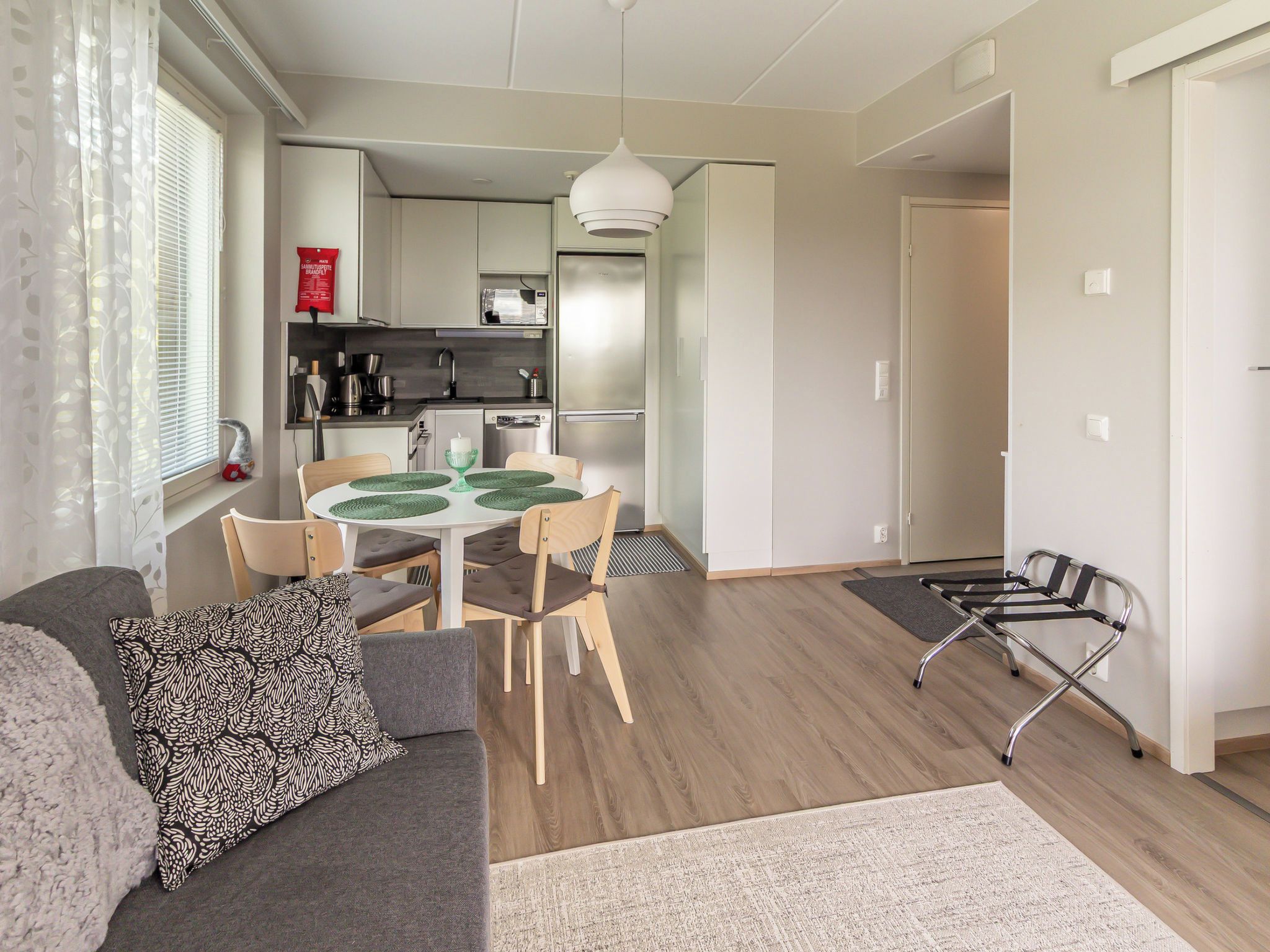 Ein modernes Wohnzimmer mit einer Couch, einem Esstisch mit Stühlen, einer Küche im Hintergrund und einem Rollstuhl.