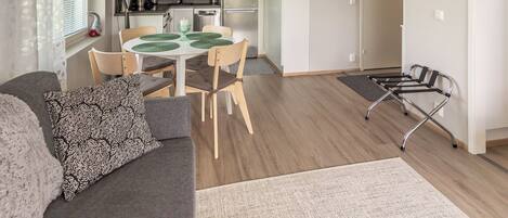 Ein modernes Wohnzimmer mit einer Couch, einem Esstisch mit Stühlen, einer Küche im Hintergrund und einem Rollstuhl.