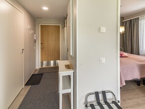 Ein Hotelzimmer mit einem Bett, einem Schreibtisch mit Stuhl, einer Tür und einem kleinen Tisch mit Notizbuch.