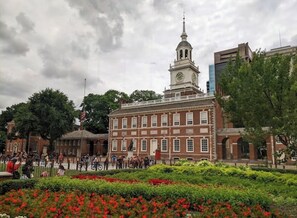 A historic building with a clock tower, surrounded by a well-maintained garden with red flowers.