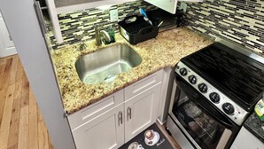 A compact kitchen with white cabinets, a granite countertop, a stainless steel sink, and a black stove. - Rental studio unit in Queen Village of Philadelphia (Philadelphia)