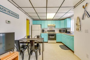 A compact kitchen with teal cabinets, a stove, microwave, and a refrigerator. There is a dining table with chairs and a television on a stand. - The Pietroman: Cottage in Sunset Bay with Fire Pit (Sunset Bay)