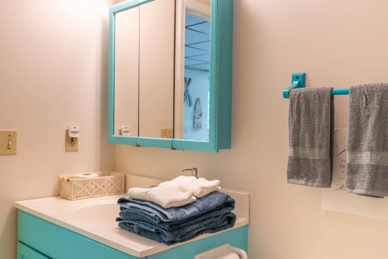 Une salle de bain avec un lavabo blanc, un miroir avec un cadre turquoise et des serviettes accrochées au mur.