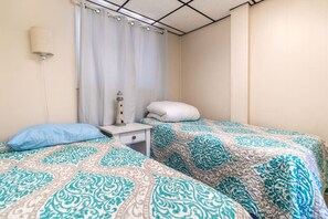 A bedroom with two beds, a nightstand, a lamp, and a curtain. - The Pietroman: Cottage in Sunset Bay with Fire Pit (Sunset Bay)
