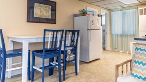 A compact kitchen with a white refrigerator, a dining table with blue chairs, and a map on the wall. - Remi-Loo's Bay Escape: Cottage in Sunset Bay (Sunset Bay)