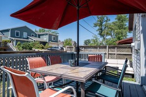 An outdoor patio with a table and chairs, a red umbrella, and a wooden deck. - Remi-Loo's Bay Escape: Cottage in Sunset Bay (Sunset Bay)