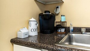 Een keuken met een koffiezetapparaat, een melkopschuimer en een koffiekan op het aanrecht.