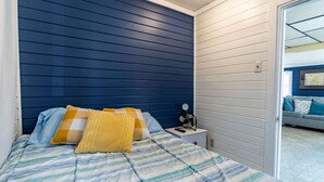 A bedroom with a bed, pillows, a bedside table with a lamp, and a view of another room. - Remi-Loo's Bay Escape: Cottage in Sunset Bay (Sunset Bay)