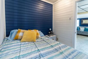 A bedroom with a bed, pillows, a bedside table with a lamp, and a view of another room. - Remi-Loo's Bay Escape: Cottage in Sunset Bay (Sunset Bay)