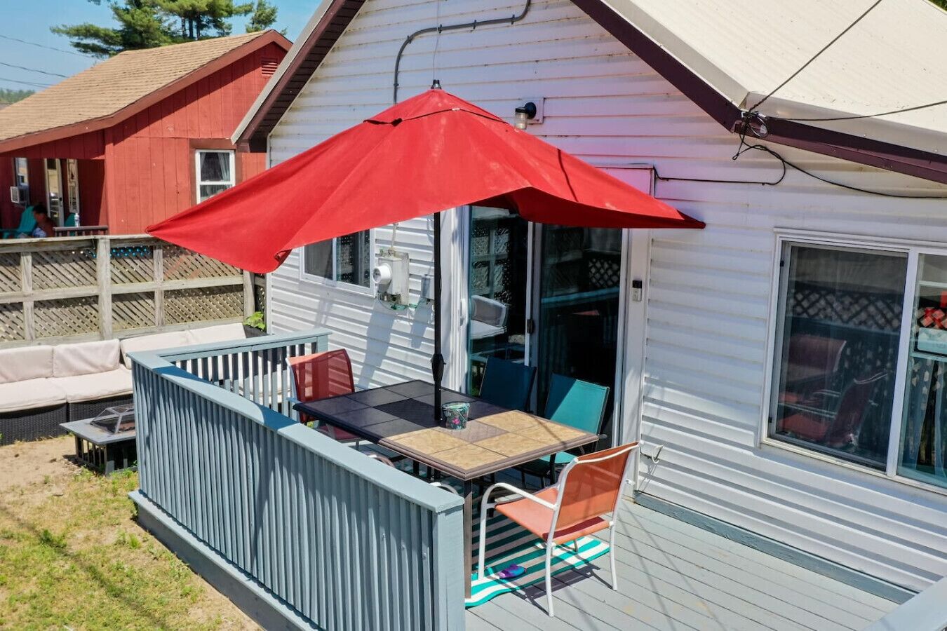 Eine überdachte Terrasse mit Tisch und Stühlen, einem roten Sonnenschirm und Blick auf ein Nachbarhaus.