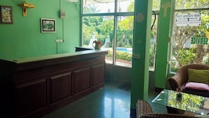 A reception area with a green wall, a wooden reception desk, and a wicker chair. - Wave point resort  (Pattaya)