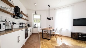 A modern kitchen with a coffee machine, a dining area with a wooden table and chairs, and a TV mounted on the wall. - FirstClass 2-room apartment (Leipzig)